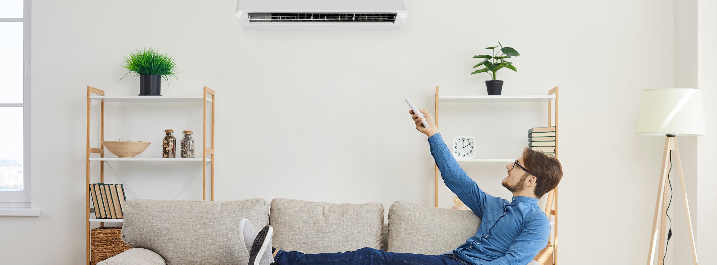 A man sits comfortably on his couch while pointing to adjust his efficient ductless heat pump.